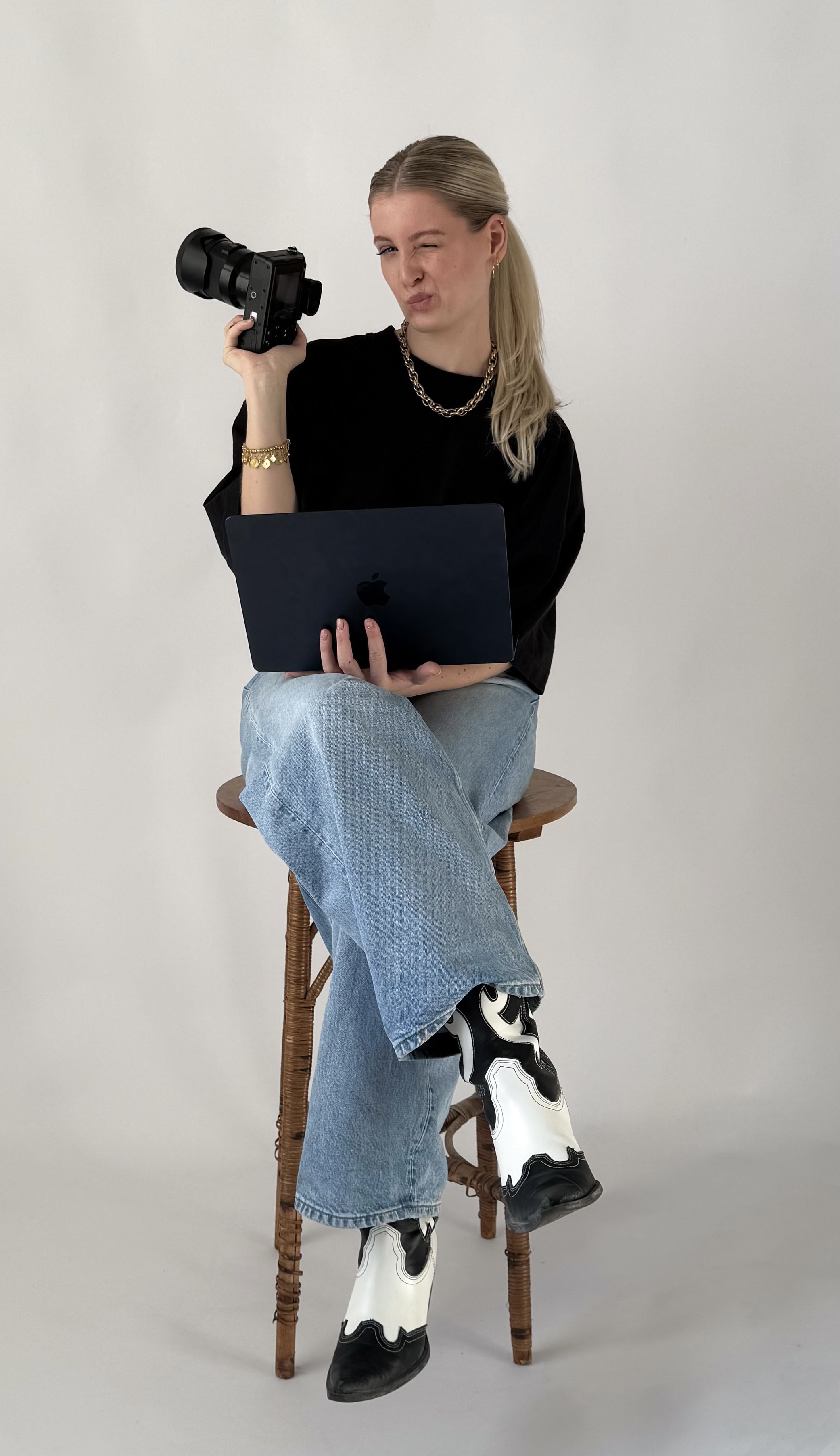 AVECK Gründerin sitzend auf einem Hocker mit Kamera und Laptop in der Hand.