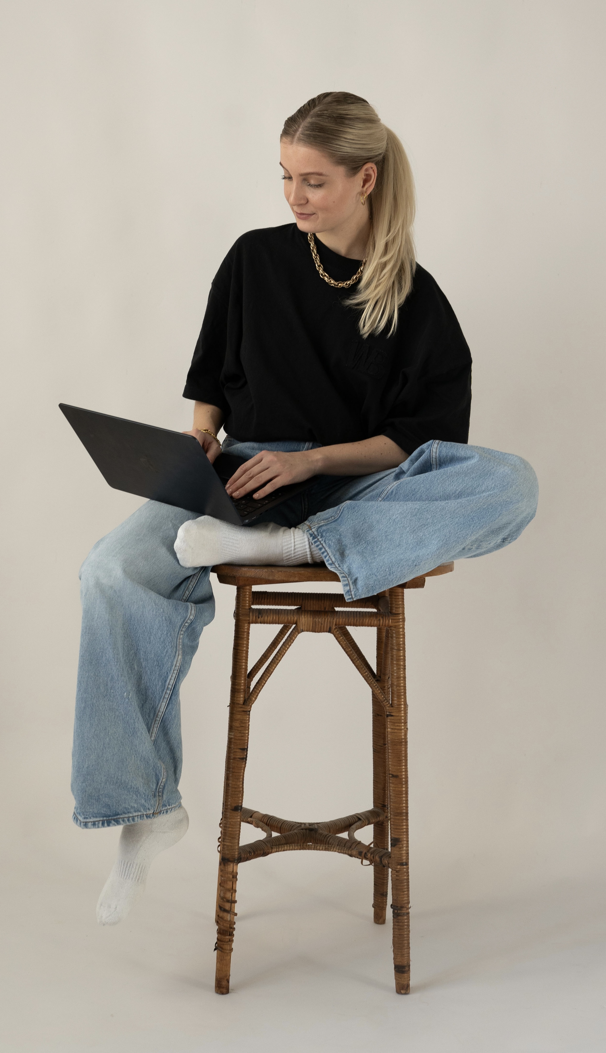 Gründerin der Agentur AVECK am Laptop - sitzend auf einem Hocker.