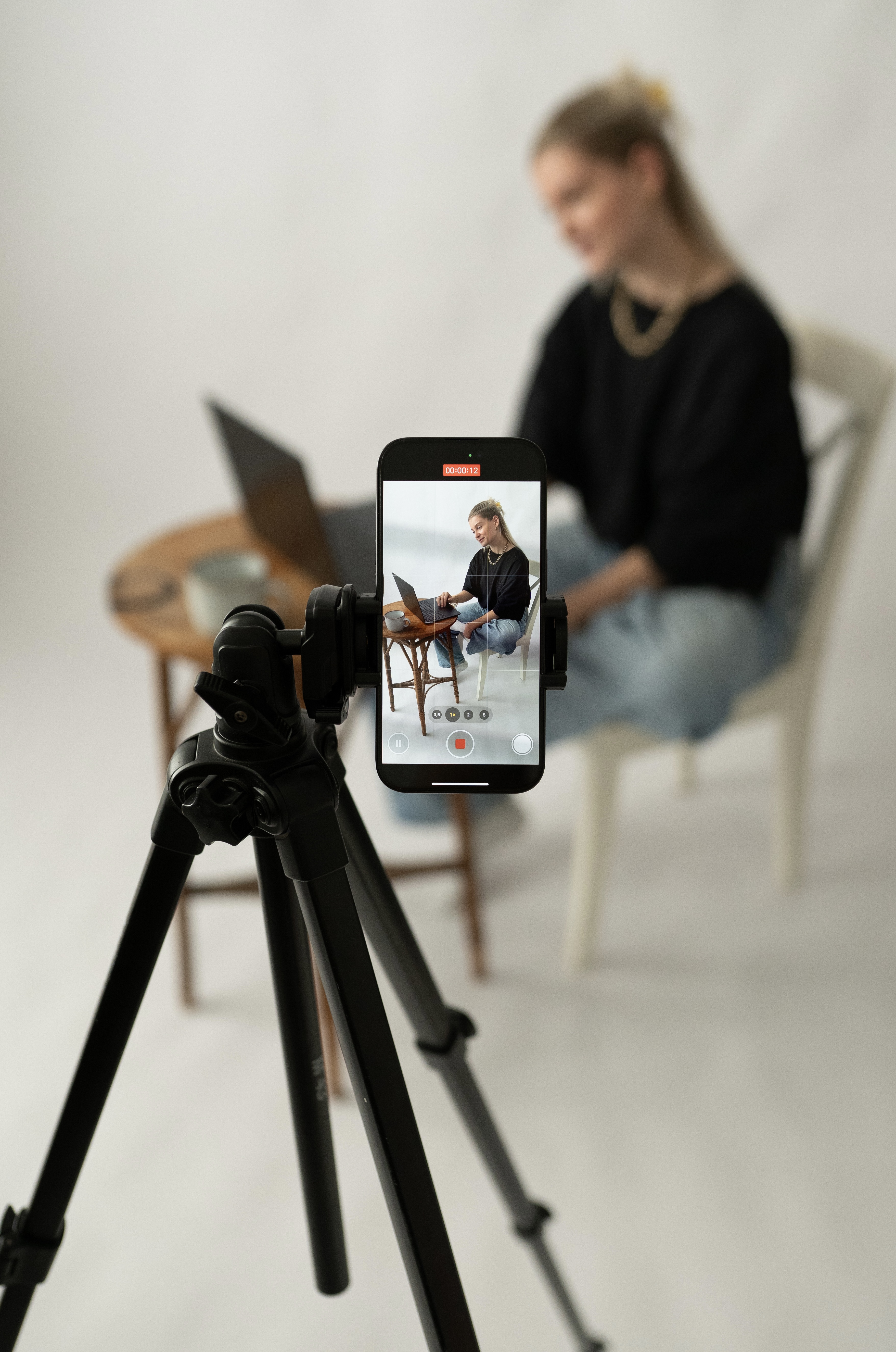 Ein Stativ mit einem Handy im Vordergrund. Dahinter AVECK Gründerin beim arbeiten zu sehen.